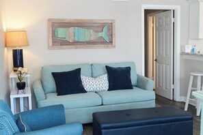 A living room with a light blue sofa, two dark blue cushions, a small side table with a lamp, and a wall-mounted fish decoration.