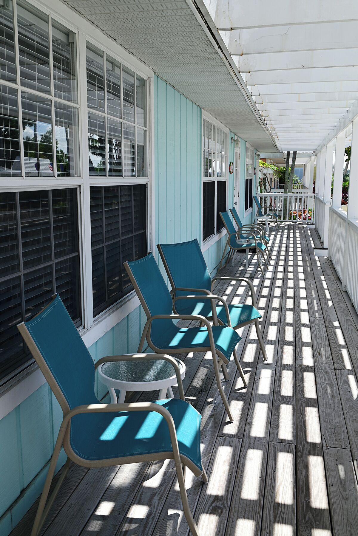 Un espace extérieur abrité, aménagé avec des rangées de chaises et de tables, une terrasse en bois et un bâtiment doté de grandes fenêtres.