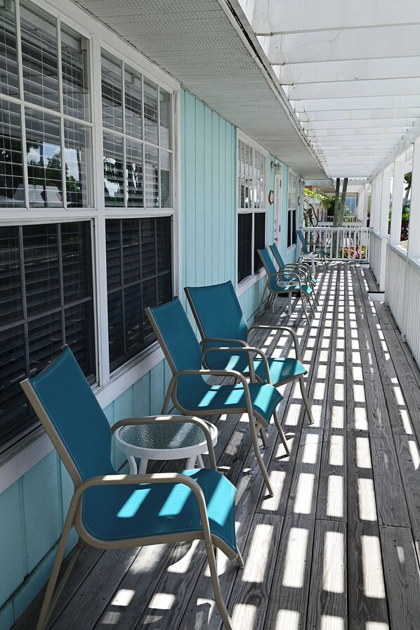 A covered outdoor seating area with rows of chairs and tables, a wooden deck, and a building with large windows.