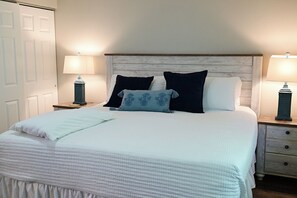 A neatly made bed with a white comforter and pillows, two bedside tables with lamps, and a wooden headboard.