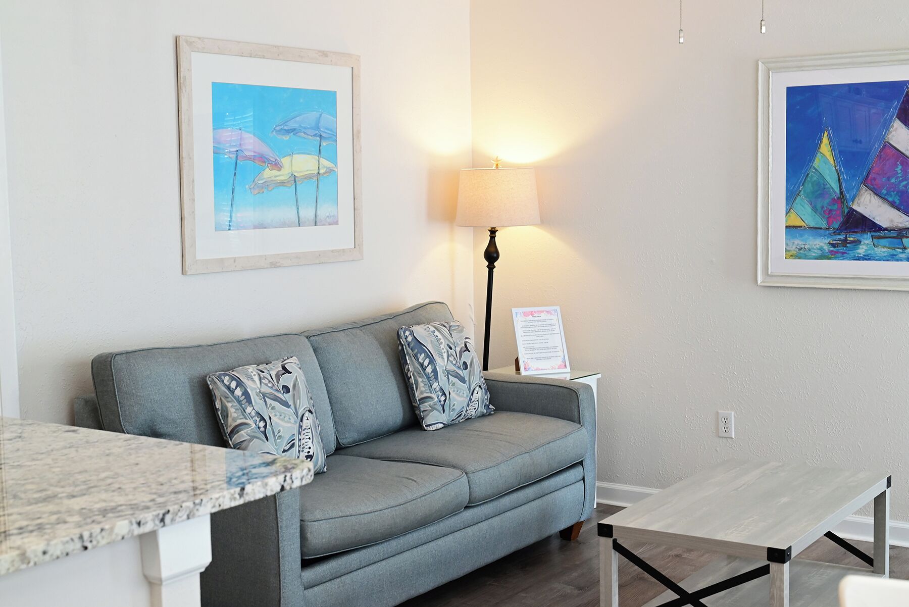 A room with a grey sofa, a small table, and two framed artworks on the walls.