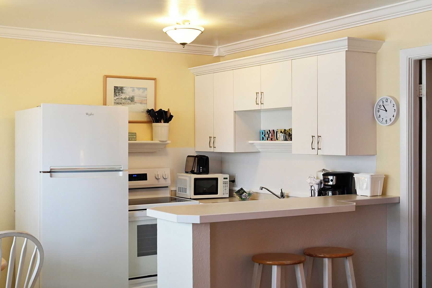 Cocina compacta con refrigerador, microondas, cafetera y un reloj en la pared.