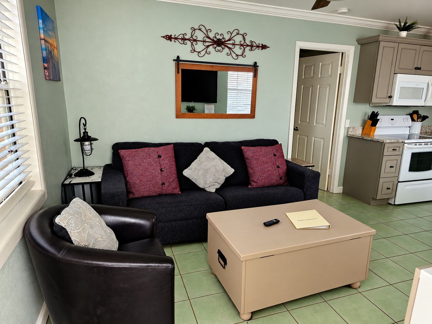 A living room with a sofa, a coffee table, a lamp, and a kitchen area with a microwave.