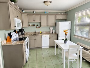 A kitchen with a dining area, including cabinets, a microwave, a refrigerator, and a table with chairs.