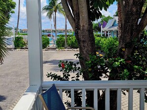 A view from a covered porch with a pool in the background, surrounded by palm trees and a clear sky.