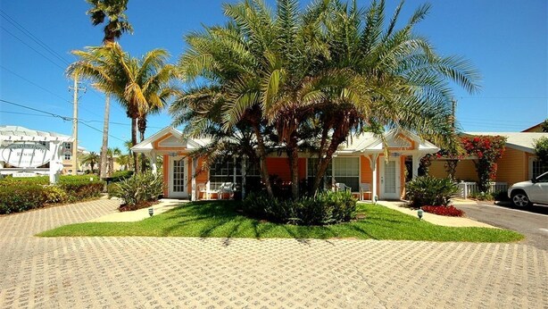 A hotel with a paved driveway, palm trees, and a building with a red and white facade. - Upgraded Coastal Style · Spacious South-Side 1 bedroom (Bradenton Beach)