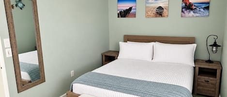 Un dormitorio con cama, un banco, una mesita de noche, una lámpara y un ventilador de techo.