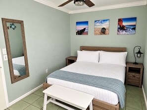 A bedroom with a bed, a bench, a nightstand, a lamp, and a ceiling fan.