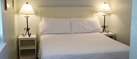 Una cama bien hecha con sábanas blancas y dos lámparas de noche a cada lado.