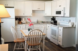 A kitchen with white cabinets, a microwave, an oven, and a dining table with chairs.