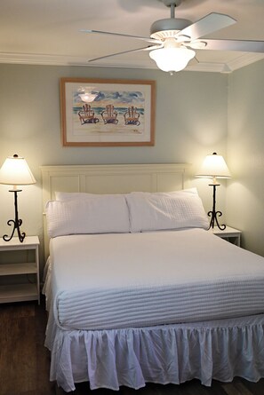 A bedroom with a bed, two bedside tables with lamps, a ceiling fan, and a framed painting on the wall.