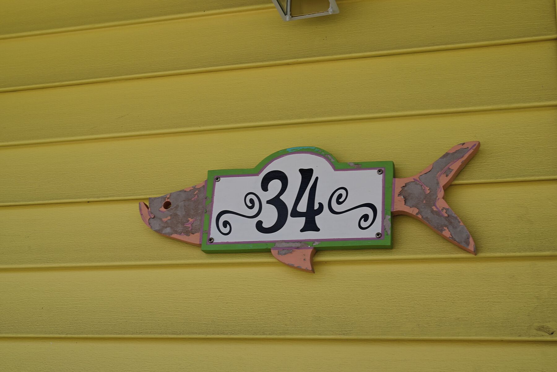A fish-shaped house number sign with the number 34 on a yellow wall.