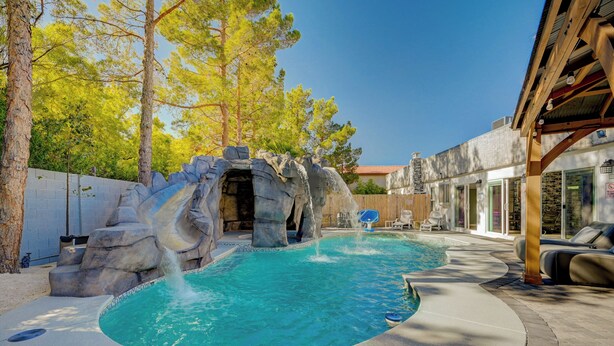 A swimming pool with a waterfall feature, surrounded by trees and a covered patio area. - Japanese Retreat (Las Vegas)