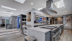 A modern kitchen with a central island, built-in ovens, and a large window above the island. - Japanese Retreat (Las Vegas)
