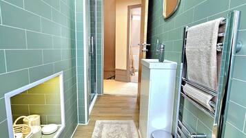 Un estrecho pasillo con paredes de azulejos verdes, un lavamanos blanco, un perchero y una puerta de madera que da a otra habitación.