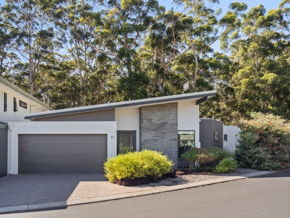 Stylish two-story residence with a modern design, surrounded by lush greenery and an entrance.
