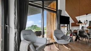 A modern living room with two grey rocking chairs, a large window with a view of greenery, a flat-screen TV mounted on the wall, and a wooden ceiling. - 3 bedroom awesome home in Tarm (Tarm)