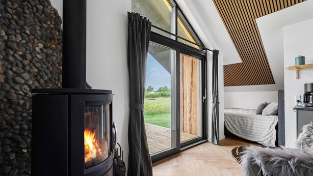 A modern living room with a wood-burning stove, a bed, and a large glass door leading to a deck. - 3 bedroom awesome home in Tarm (Tarm)