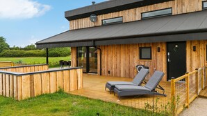 A modern building with a wooden exterior, a covered deck with two lounge chairs, and a glass door leading to a pool area. - 3 bedroom awesome home in Tarm (Tarm)