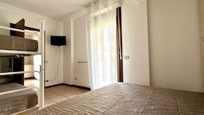 A room with bunk beds, a flat-screen TV, a radiator, and a window with curtains. - SE097 - Senigallia, two-room apartment with garden (Senigallia)