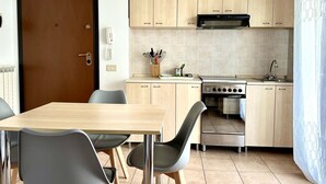 A compact kitchen with a stove, oven, and sink, a dining table with chairs, and light wooden cabinets. - SE097 - Senigallia, two-room apartment with garden (Senigallia)
