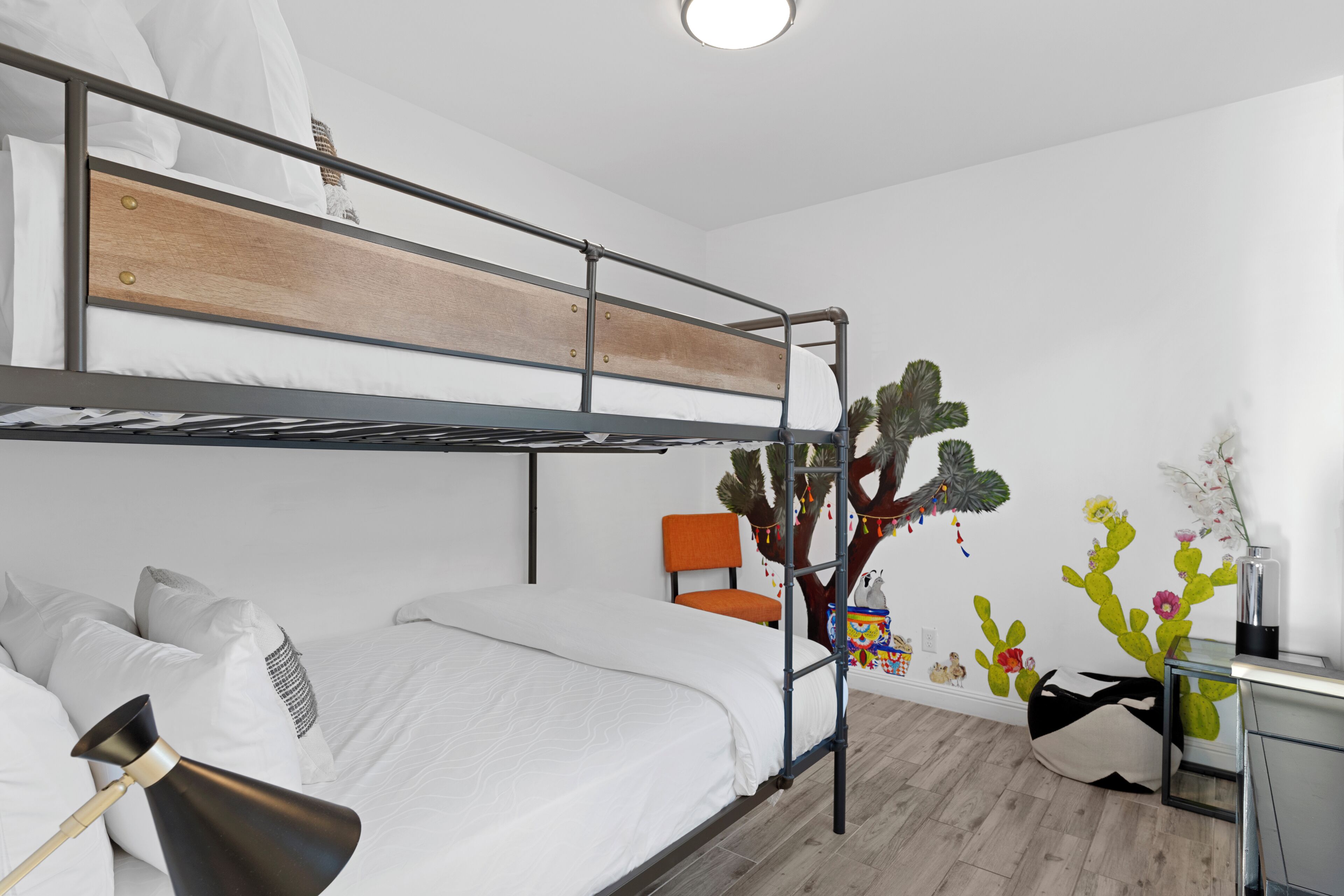 A bunk bed room with a desk, a chair, and a cactus wall decal.