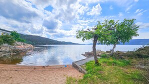 A lakeside beach with a wooden dock, a tree, and a distant mountain range. - Nice home in Klokkarstua with WiFi (Klokkarstua)
