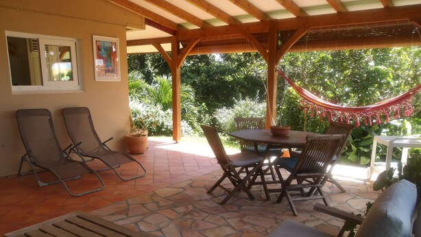 A covered patio with stone flooring, wooden furniture, and a hammock. - Large T2 ground floor In the countryside of Fort de France (Fort-de-France)