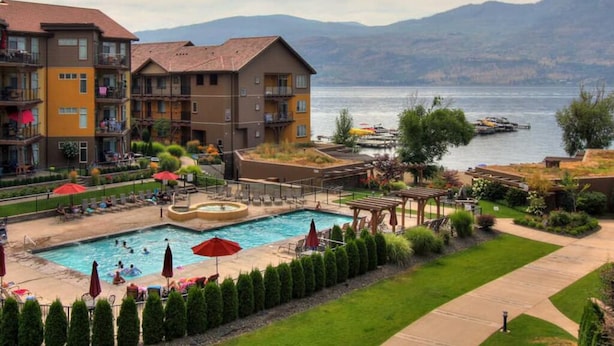 Un hotel con piscina, mobiliario exterior y vistas a un lago y montañas.