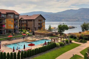 A hotel with a swimming pool, outdoor seating, and a view of a lake and mountains. - **LAKEFRONT + POOL VIEW**  3br/2bath Spacious + Beautiful Condo  (West Kelowna)