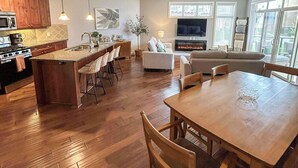 Una cocina amplia con armarios de madera y una isla central, un comedor con mesa y sillas de madera, y una sala de estar con chimenea y un televisor grande.