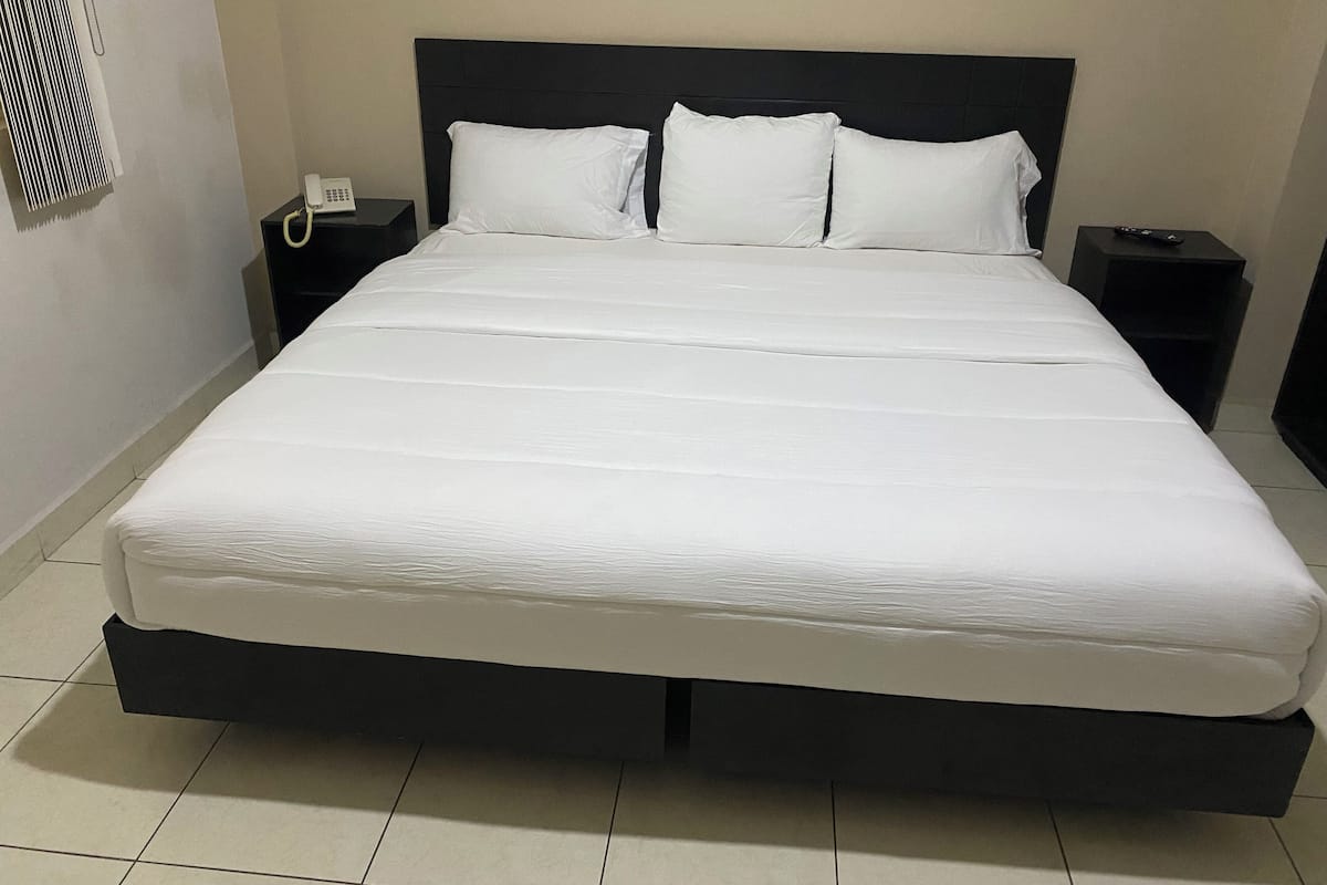 Ein großes Bett mit schwarzem Kopfteil, weißer Bettwäsche und zwei Nachttischen mit Telefon und Fernbedienung.