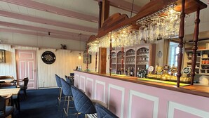 Angolo bar con travi in legno, bancone con vetrina e diversi sgabelli da bar.