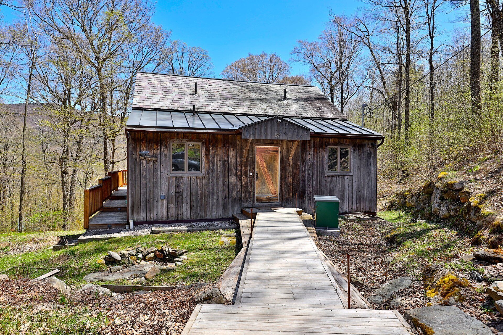 A rustic cabin with a wooden exterior, a metal roof, and a wooden deck leading to the entrance.
