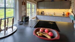 Ett kök med ett stort fönster, en brödrost, en vattenkokare och en skål med frukt på bänkskivan.