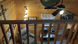 L’intérieur d’une cabane en bois, avec un ventilateur de plafond, des lampes suspendues et un tableau encadré accroché au mur.