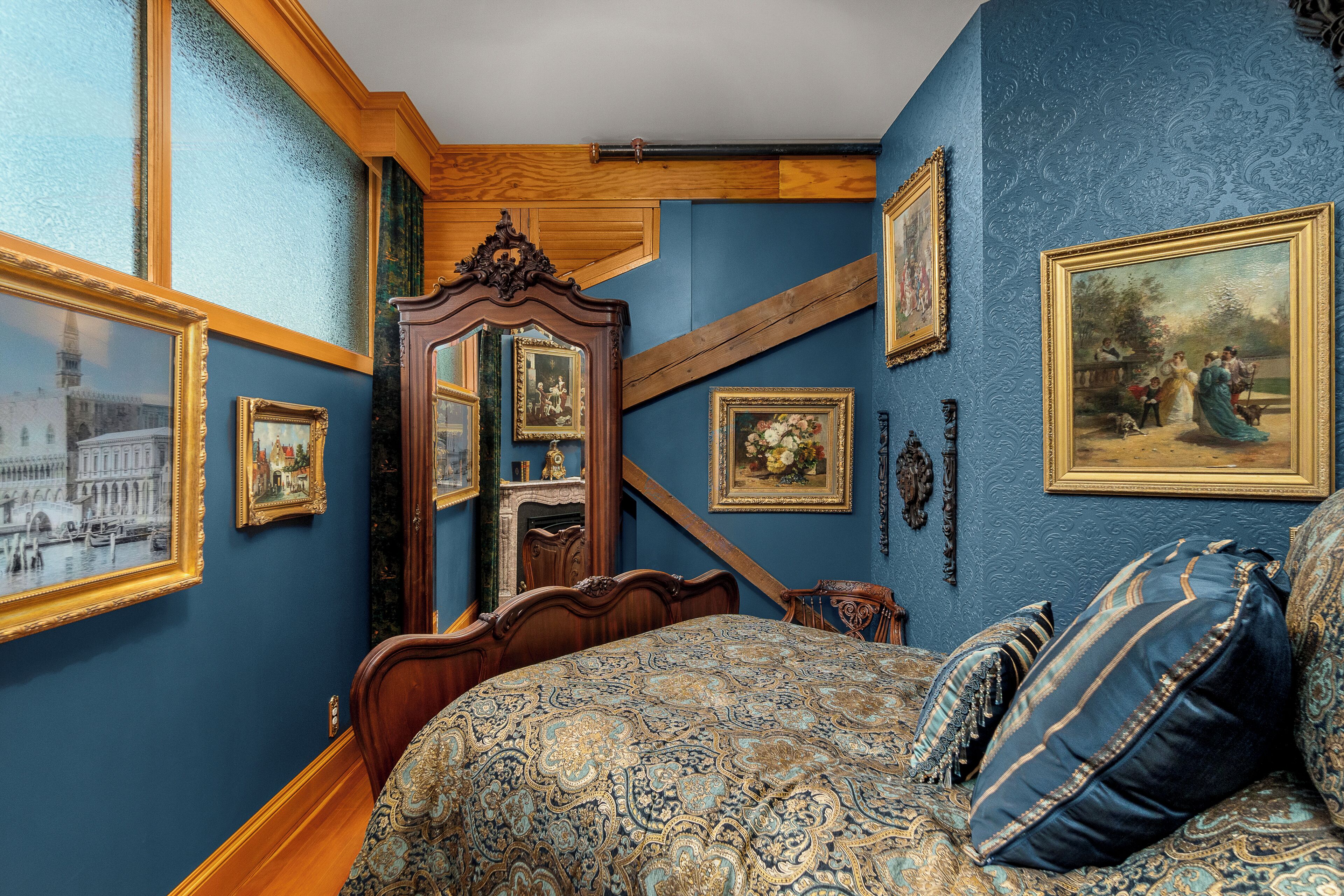 A bedroom with a large bed, a wooden wardrobe, and several framed pictures on the walls.