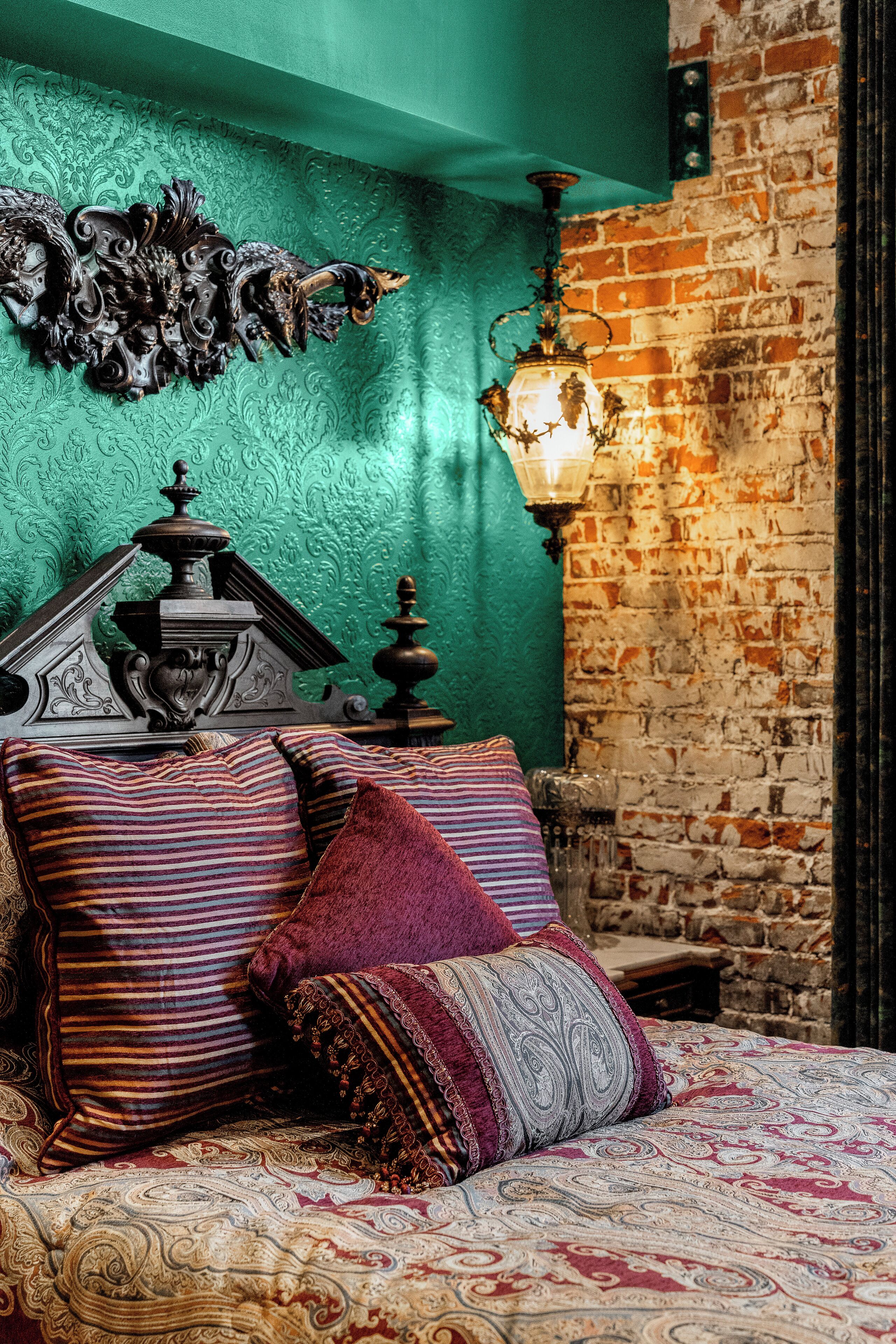 Un letto con biancheria a motivi, una testiera decorativa e una lampada a parete.