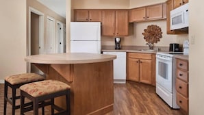 A kitchen with wooden cabinets, a white refrigerator, a microwave, a stove, and two bar stools with floral upholstery. - WorldMark Big Bear - 1 Bedroom Accessible (Big Bear)