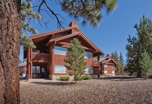 A two-story wooden cabin with a balcony, surrounded by pine trees and a gravel driveway. - Big Bear | Couples Cozy Mountain Getaway | Pool, Ski & Lake (Big Bear)