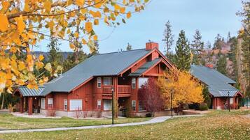 A two-story wooden cabin with a metal roof, surrounded by a well-maintained lawn and autumn foliage.