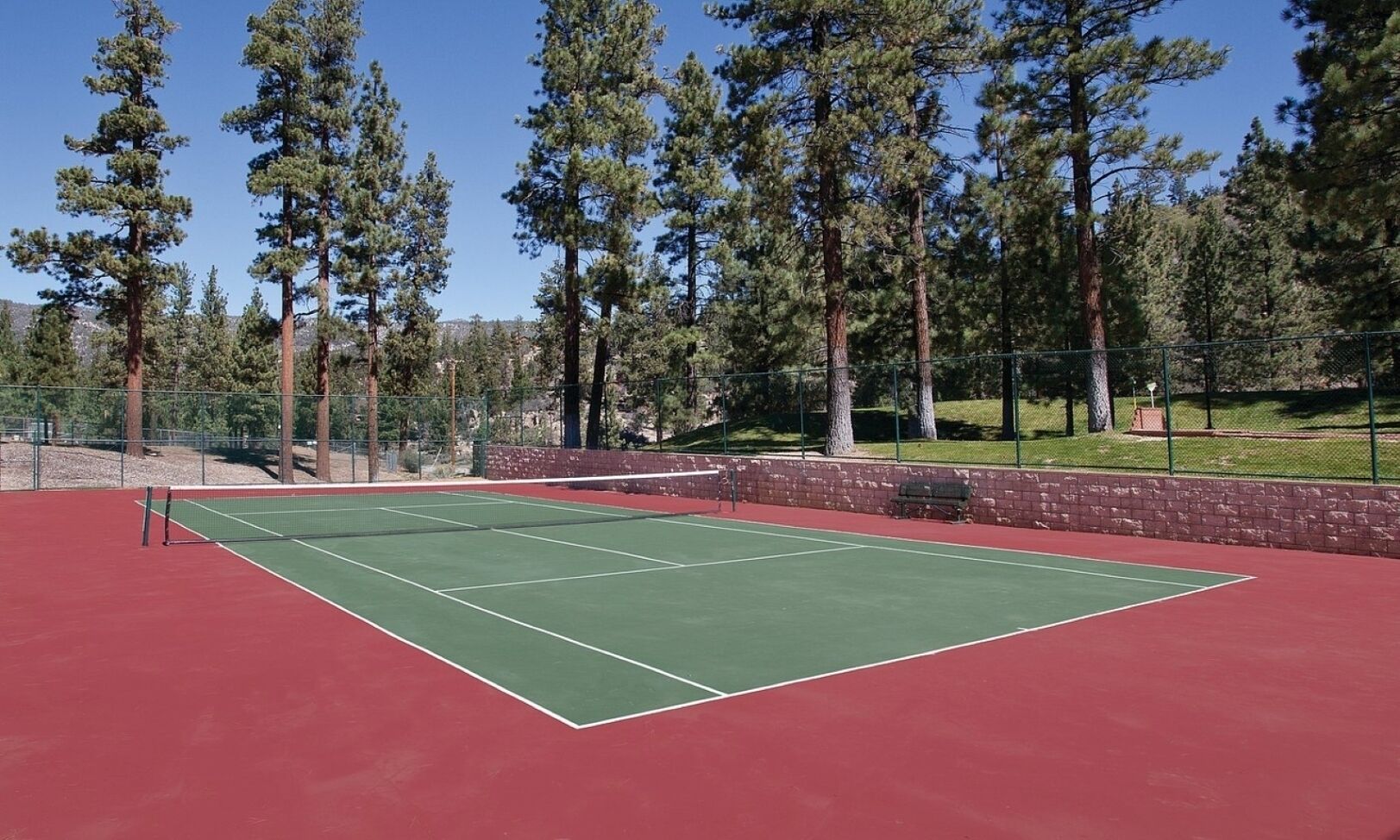 A tennis court with a red surface, surrounded by a fence and trees.