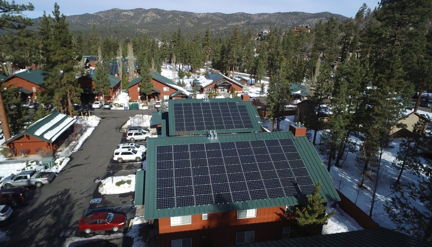 A resort with multiple cabins, solar panels on roofs, a parking area, and a mountainous backdrop.