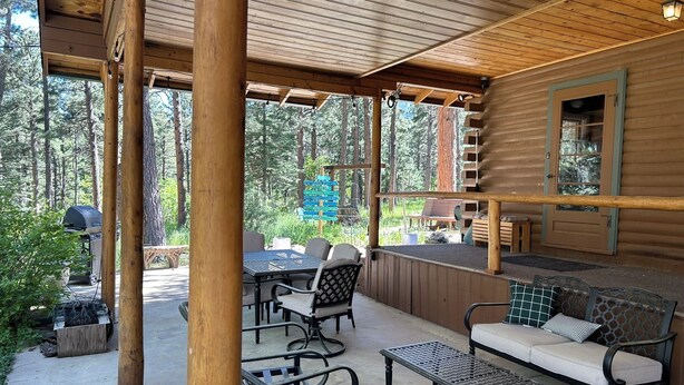 Un espacio al aire libre con techo, muebles de madera, una parrilla y vistas al bosque.