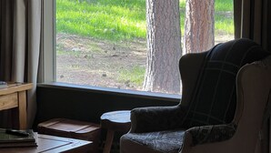 Una habitación con un ventanal grande, un escritorio de madera, una silla y una mesita.