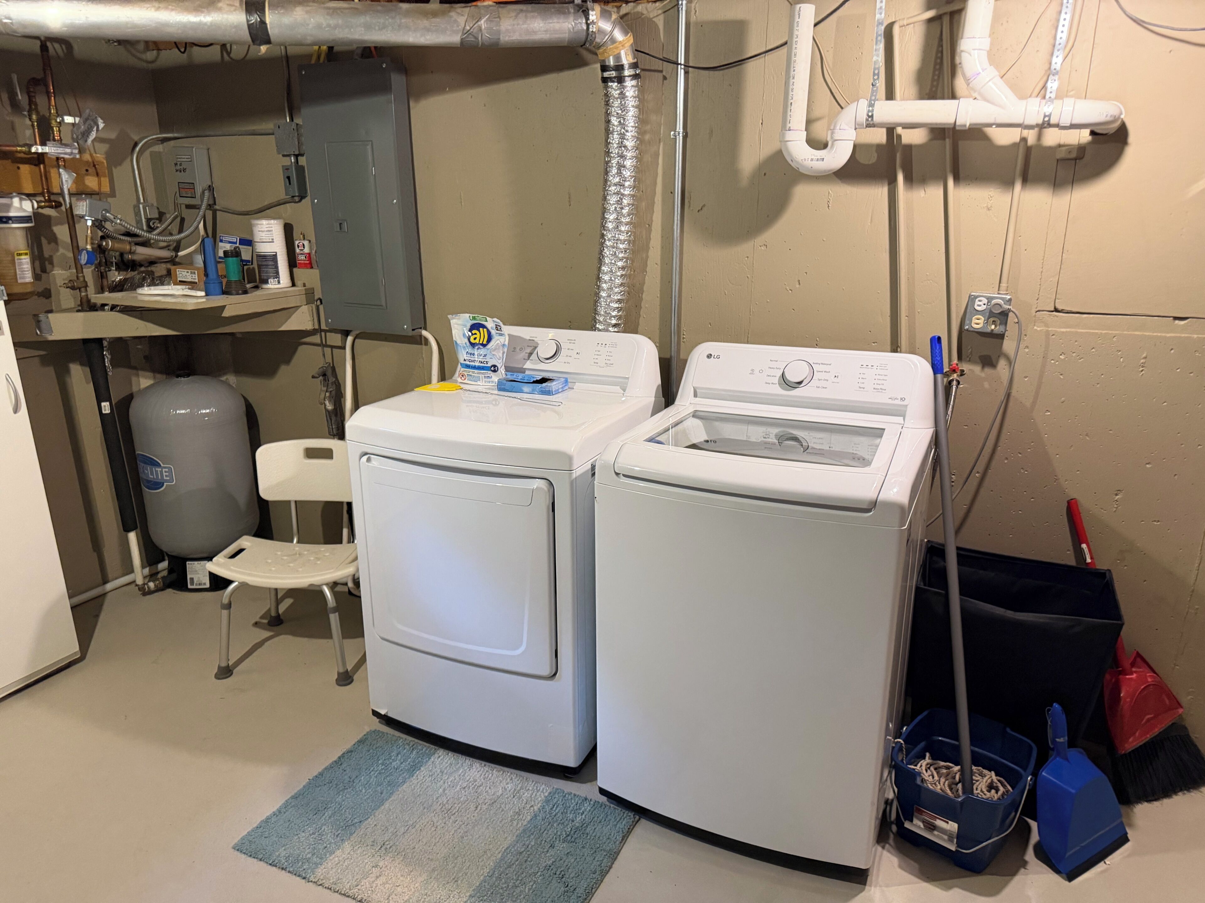 A laundry room with two front-loading washers, a water heater, and a small chair.
