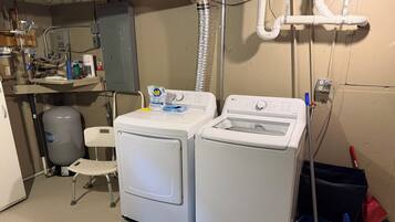 A laundry room with two front-loading washers, a water heater, and a small chair.