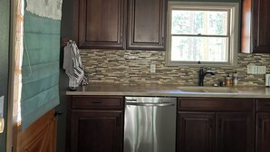 Una cocina con armarios de madera oscura, lavavajillas de acero inoxidable y ventana con vista a árboles.