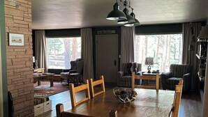 Un comedor con una mesa y sillas de madera, un muro de piedra y vistas a árboles a través de amplios ventanales.
