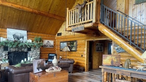 A log cabin interior with a fireplace, leather furniture, and a stone wall.